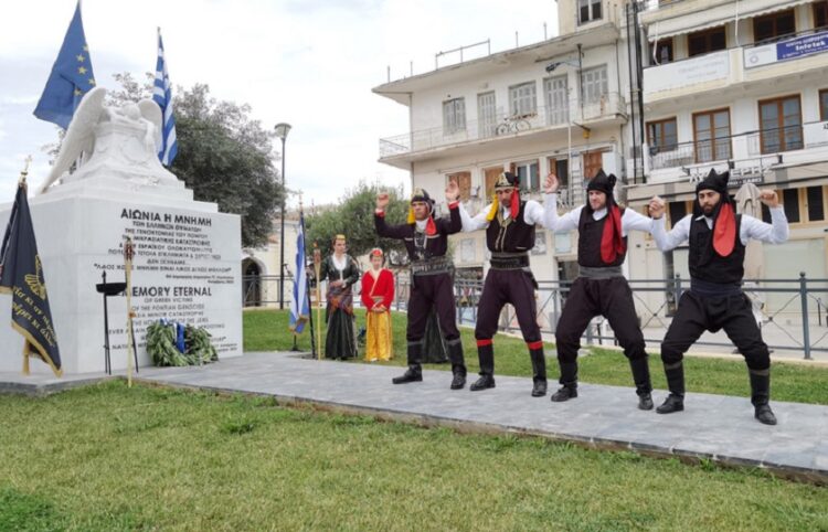 Πυρριχιστές αποδίδουν το χορό σέρρα δίπλα στο μνημείο που βρίσκεται στο Άργος, στην Πλατεία Δημοκρατίας (φωτ.: ΑΠΕ-ΜΠΕ / Ευάγγελος Μπουγιώτης)