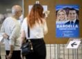 Γάλλοι ψηφοφόροι μπροστά σε προεκλογική αφίσα της Μαρίν Λεπέν και του επικεφαλής του ακροδεξιού κόμματος «Εθνικός Συναγερμός» Ζορντάν Μπαρντελά (φωτ.: EPA/Laurent Gillieron)