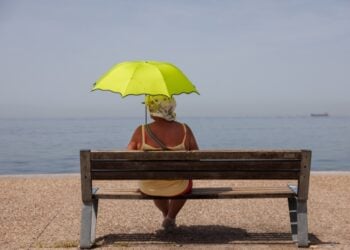 Μία γυναίκα σε παγκάκι κρατά ομπρέλα για να προστατευθεί από τον ήλιο στην παραλία της Θεσσαλονίκης (φωτ.: ΑΠΕ-ΜΠΕ/Αχιλλέας Χήρας)