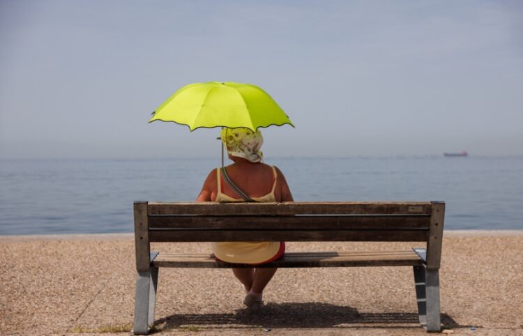 Μία γυναίκα σε παγκάκι κρατά ομπρέλα για να προστατευθεί από τον ήλιο στην παραλία της Θεσσαλονίκης (φωτ.: ΑΠΕ-ΜΠΕ/Αχιλλέας Χήρας)