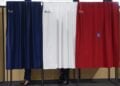 Ο Εμανουέλ Μακρόν και η σύζυγός του πίσω από το παραβάν με τα χρώματα της γαλλικής σημαίας, κατά τη διάρκεια της ψηφοφορίας για τον β' γύρο των γαλλικών βουλευτικών εκλογών (φωτ.: EPA / Mohammed Badra / Pool)