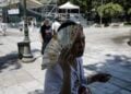 Γυναίκα χρησιμοποιεί τη βεντάλια της για να καλυφθεί από τον ήλιο καθώς διασχίζει την πλατεία Συντάγματος (φωτ.: ΑΠΕ-ΜΠΕ / Κώστας Τσιρώνης)