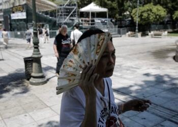 Γυναίκα χρησιμοποιεί τη βεντάλια της για να καλυφθεί από τον ήλιο καθώς διασχίζει την πλατεία Συντάγματος (φωτ.: ΑΠΕ-ΜΠΕ / Κώστας Τσιρώνης)