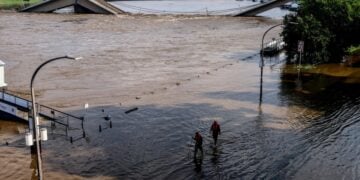 Εργαζόμενοι περνούν μέσα από πλημμυρισμένο ποτάμι στη Δρέσδη της Γερμανίας, ενώ πίσω τους διακρίνεται μια σπασμένη γέφυρα (φωτ.: EPA/Filip Singer)