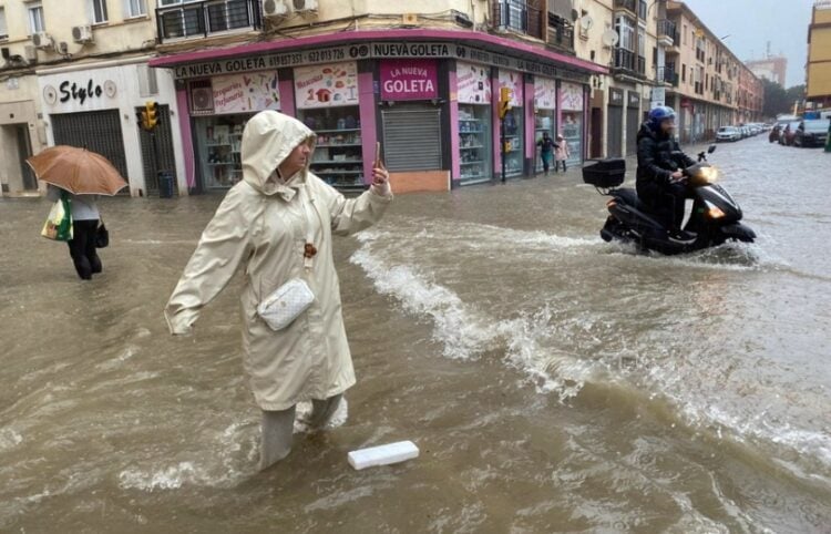 Γυναίκα βγάζει φωτογραφία σε πλημμυρισμένο δρόμο της Μάλαγα, η οποία είναι σε κόκκινο συναγερμό λόγω εξαιρετικά έντονης βροχόπτωσης (φωτ.: EPA/Maria Alonso)