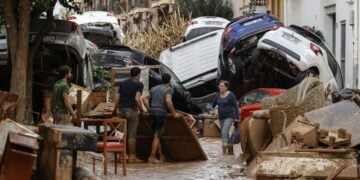 Πολίτες προσπαθούν να καθαρίσουν περιοχή στη Βαλένθια, ενώ πίσω τους βρίσκονται παρασυρμένα αυτοκίνητα από τις πλημμύρες της Τετάρτης (φωτ.: EPA/Biel Alino)