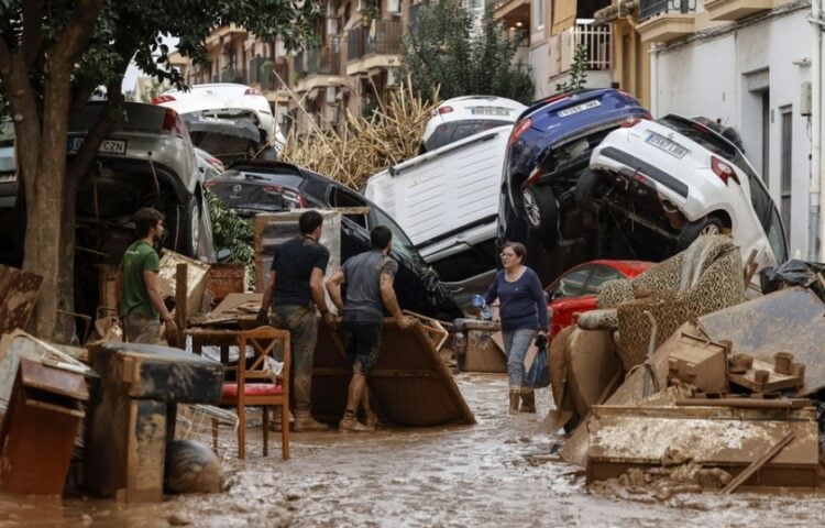 Πολίτες προσπαθούν να καθαρίσουν περιοχή στη Βαλένθια, ενώ πίσω τους βρίσκονται παρασυρμένα αυτοκίνητα από τις πλημμύρες της Τετάρτης (φωτ.: EPA/Biel Alino)